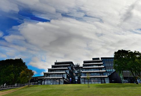 Exterior of glass terraced Checkland building against dramatic summer clouds, Falmer Campus